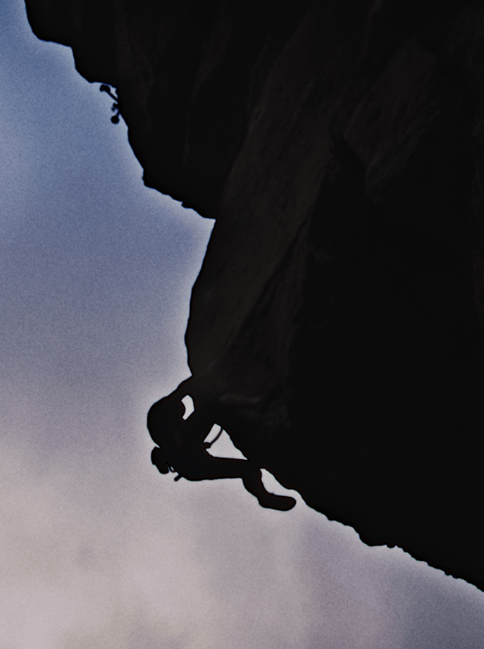 Silueta de un escalador ascendiendo por una pared de roca escarpada en Tenerife bajo un cielo dramático, ejemplificando el espíritu de aventura de la campaña Gen Explorador.