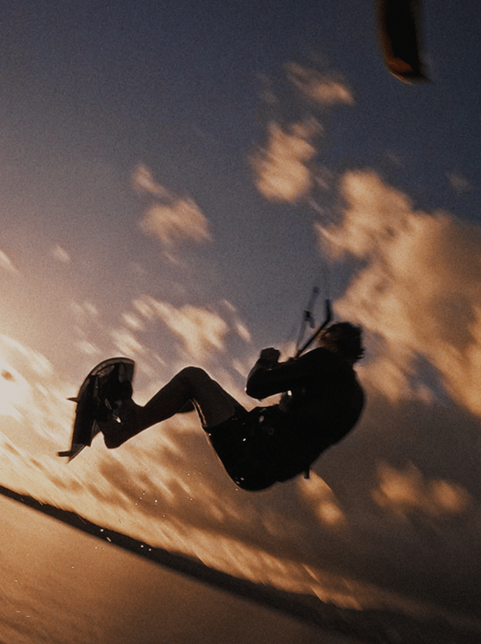 Un deportista realizando un salto de kitesurf sobre las olas en Tenerife durante el atardecer, bajo un cielo de tonos cálidos y nubes dramáticas.