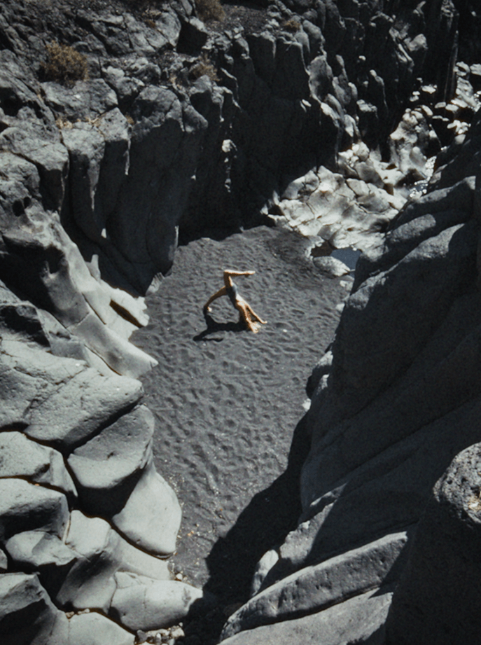Una persona realizando una postura de yoga sobre arena negra entre formaciones de roca volcánica en un paraje natural de Tenerife, representando las experiencias de bienestar de la campaña Gen Explorador.